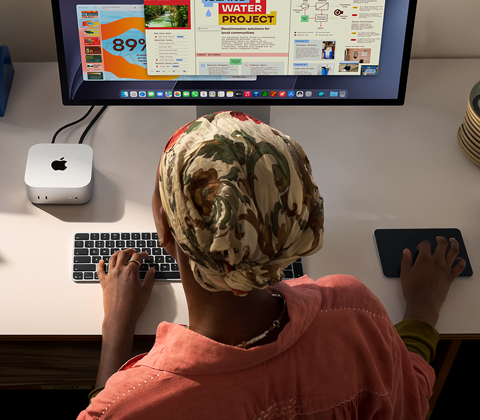 Iemand die typt aan een bureau met een Mac mini, Studio Display aangesloten, Magic Keyboard, Magic Trackpad, diverse items