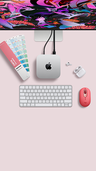 Bovenkant van Mac mini, zilverkleurig aluminium, afgeronde hoeken, glanzend zwart Apple logo in het midden, verbonden met een kabel, Studio Display deels zichtbaar aan de bovenkant, AirPods 4, opengeklapt, Pantone-kleurstalen, en Logitech-toetsenbord en -muis in rode kleur