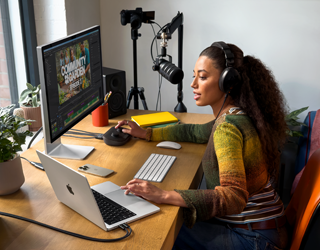 Een vrouw werkt thuis aan haar bureau met een MacBook Pro die is verbonden met twee externe displays, ze draagt oortjes en praat in een microfoon